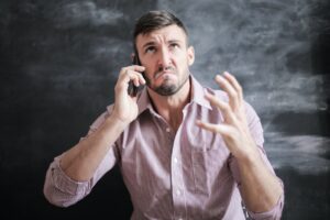 A frustrated man holds a phone and frowns